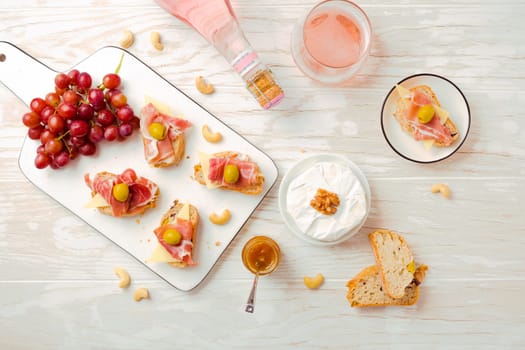 Flat lay of Appetizers and open sandwiches with Italian antipasti, camembert, Parma ham and rose wine on wooden table