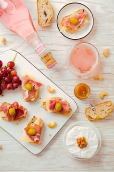 Flat lay of Appetizers and open sandwiches with Italian antipasti, camembert, Parma ham and rose wine on wooden table