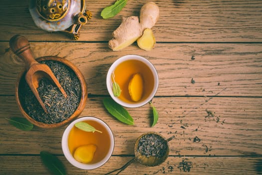 Ginger tea with sage leaves and dried black tea leaves on wooden background