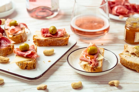 Appetizers and open sandwiches with Italian antipasti, camembert, Parma ham and rose wine on wooden table