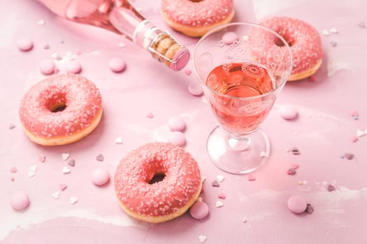 Rose wine or cocktail with pink donuts and pink chocolate beans on pink background