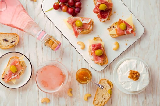 Flat lay of Appetizers and open sandwiches with Italian antipasti, camembert, Parma ham and rose wine on wooden table