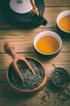 Black tea with dried tea leaves and infuseron wooden background