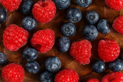 Detail top view on mixed blueberries and raspberries on wooden plate.