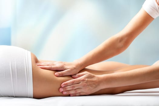 Therapist massaging upper back part of female leg. Hands applying pressure on hamstrings.