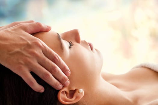 Close up head portrait of young woman having facial massage in spa. Therapist massaging woman’s head against colorful background.