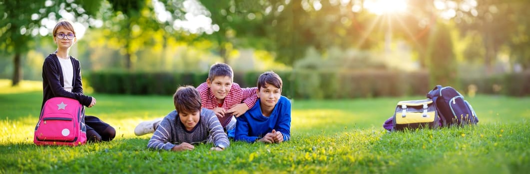 Children with rucksacks standing in the park near school. Pupils with books and backpacks outdoors lying on the grass