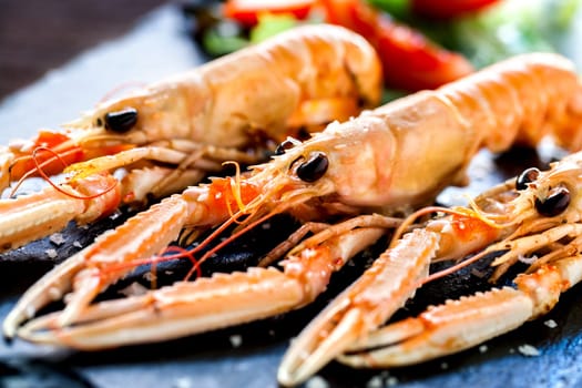 Macro close up of appetizing grilled giant crawfish platter with green salad in backround..