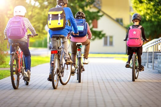 Children with rucksacks riding on bikes in the park near school. Pupils with backpacks outdoors