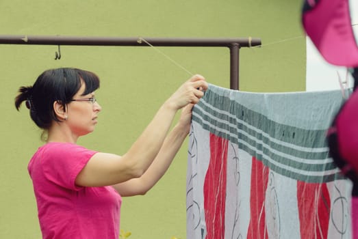 Caucasian woman hanging freshly washed laundry to dry on clothesline in the sun on at summer or spring season, saving energy concept.