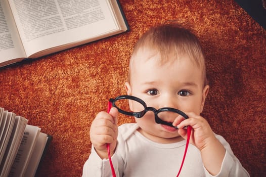One year old baby among books with spectackles.Happy little child reading