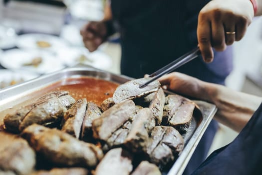 A baking tray with roasted meat. Take a piece of meat to taste.
