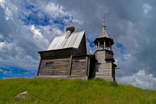 A wooden church on a green hill. Grass on the choir outside the church.