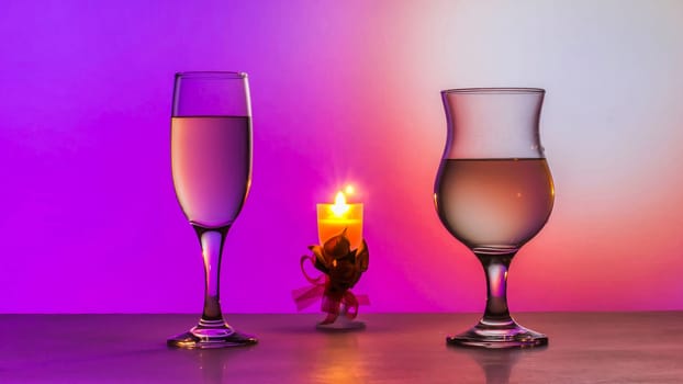 Two glasses of white wine and a candle on the table. Pink background.