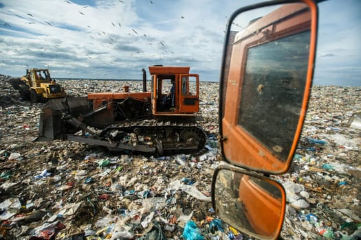 Work of special equipment at the pumping range. Bulldozers are clearing up the garbage. Seagulls over the landfill.