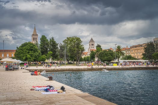 Zadar, Croatia, July 2019 Crowds of tourists walking and relaxing on the Coast of King Petar Kresimir IV. People playing water polo in Adriatic Sea