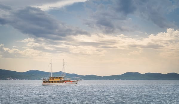 Sailboat or yacht sailing on Adriatic Sea at sunset. Coastline with mountain range seen from Zadar bay, Croatia