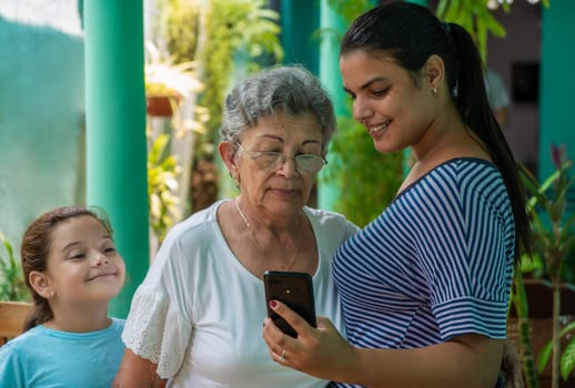 Young woman showing a cell phone to an old woman and a girl looking too
