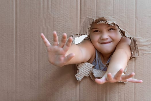 Girl behind a cardboard with her arms stretched forward through the cardboard