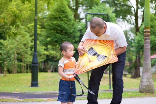 Father teaching son to fly a kite at outdoor garden park. Happy Southeast Asian family living lifestyle.