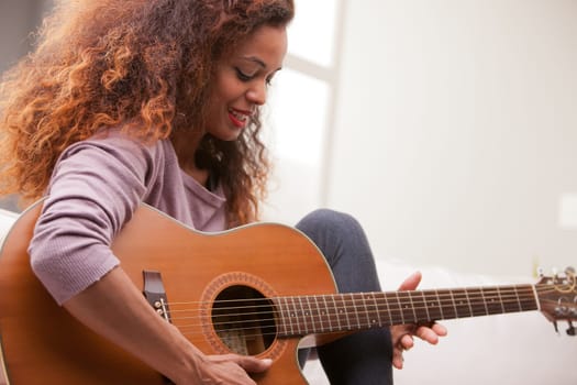 afroamerican woman singing and playing guitar on her sofa in her living room