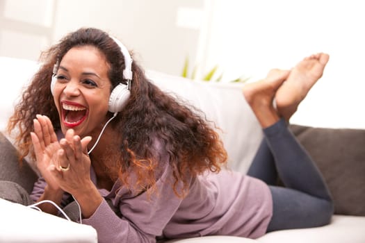 african american woman singing on a sofa wearing white headphones