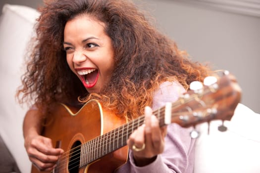 afroamerican woman singing and playing guitar on her sofa in her living room