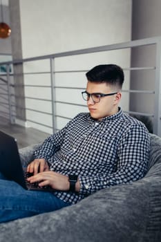 Man using laptop, wearing glasses, cushioned furniture. Blurred background. High quality photo