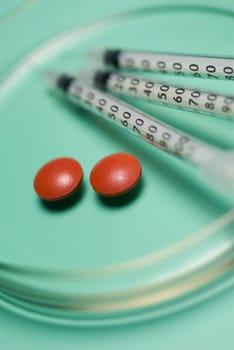 Close_up of three syringes with pills in a petri dish