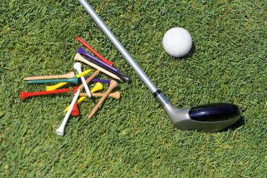 Close-up of a golf club with a golf ball and tees on the grass