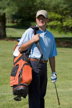 Mature man standing on a golf course carrying a golf bag with a golf club