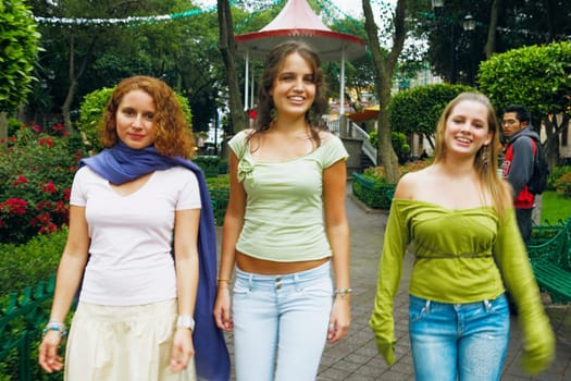 Three young women walking on a walkway in a park