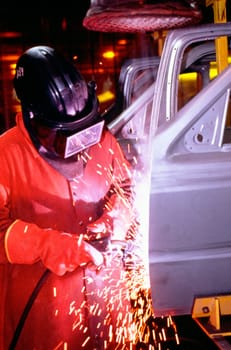 Automobile factory mechanic working on chassis in a shower of sparks