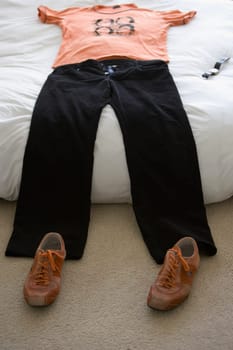 T-shirt and jeans on the bed with a pair of shoes on the floor