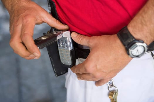 Mid section view of a man fastening a mobile phone on his belt
