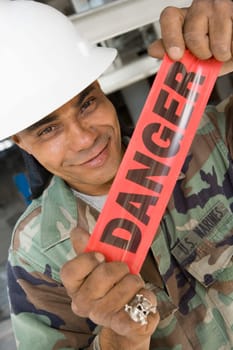 Portrait of a male construction worker holding a cordon tape and smirking