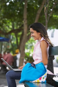 Side profile of a young woman sitting on a bench and using a laptop, Old San Juan, San Juan, Puerto Rico
