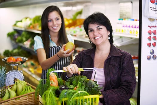 Portrait of a mature woman holding a shopping basket and a female sales clerk giving her a mango