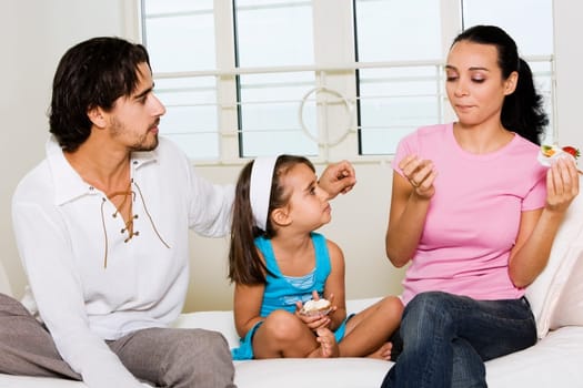 Close-up of a young woman sitting holding a pastry with her daughter and a young man