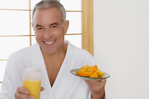 Portrait of a senior man holding a plate of oranges and a glass of orange juice