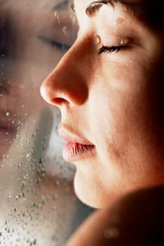 Close-up of a young woman with her face against a glass window