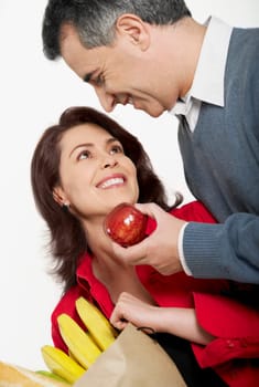 Close-up of a mid adult man holding an apple with a mid adult woman holding a shopping bag beside her