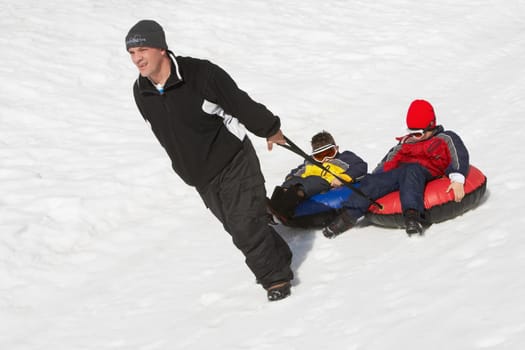 Mature man pulling his two children sitting on inner tubes