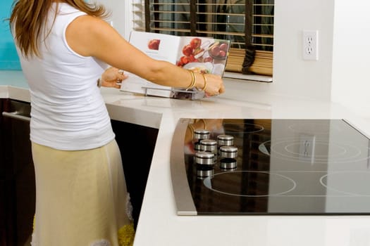Mature woman reading a cookbook at a kitchen counter