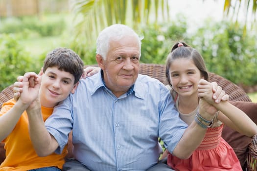 Portrait of a senior man holding his grandchildrenŽs hands and smiling