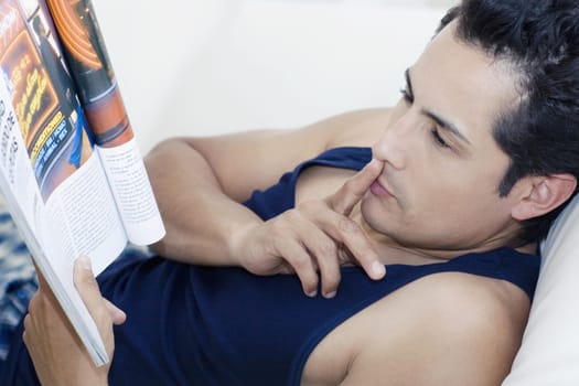 Side profile of a young man reading a magazine with his finger on his lips