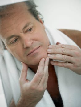 Reflection of a mature man touching his face in a mirror