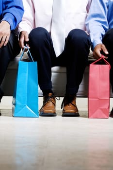 Low section view of three people sitting on a couch holding shopping bags