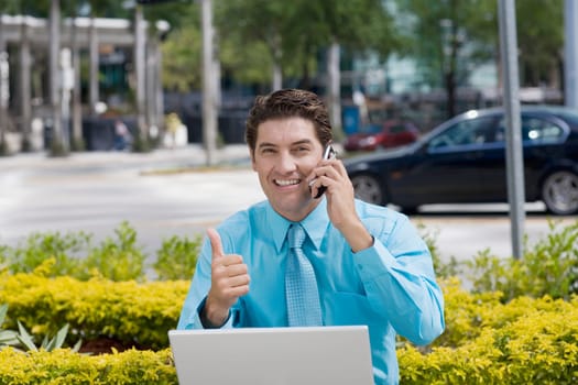 Portrait of a businessman talking on a mobile phone and showing a thumbs up sign