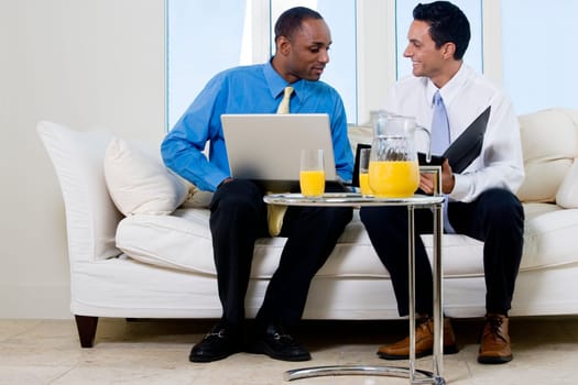 Two businessmen sitting on a couch holding a file and a laptop